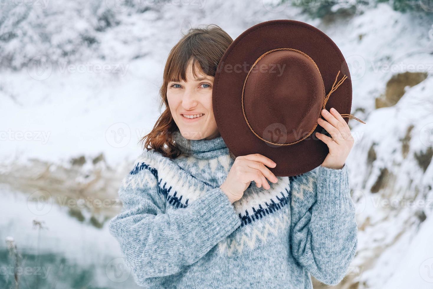 Portrait of a smiling woman in a brown hat and sweater on a background of winter landscape photo