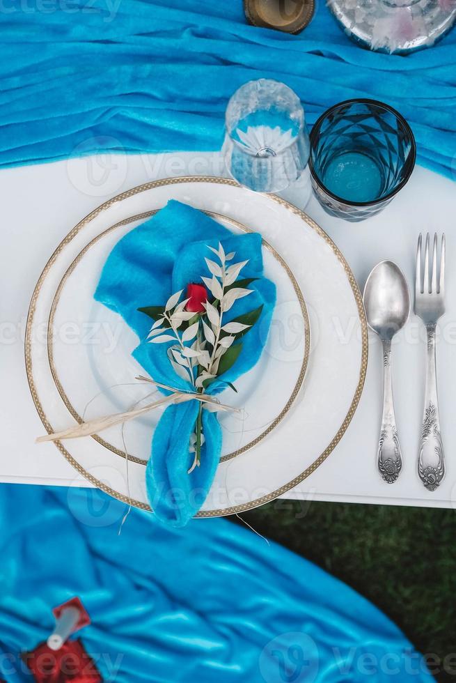 White banquet table covered with blue cloth, served with plates, cutlery, glasses, candles and flower arrangements. Top view. Copy, empty space for text photo