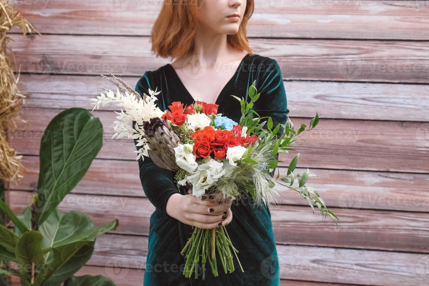 Beautiful girl in a green dress holding a bouquet of flowers and greenery on a wooden background. Copy, empty space for text photo