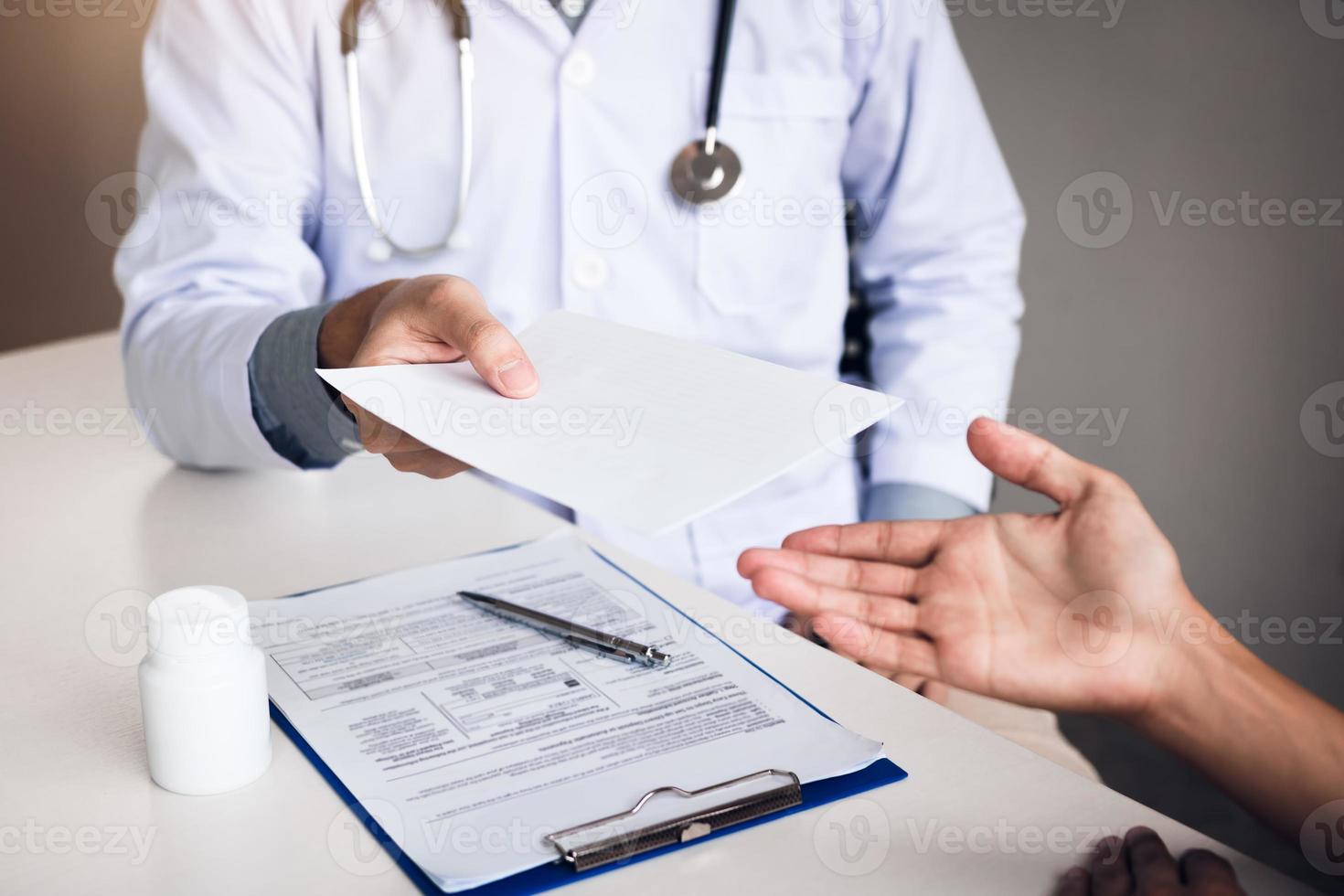 Asian male doctor talking in clinic room and handing a prescription to the patient. photo