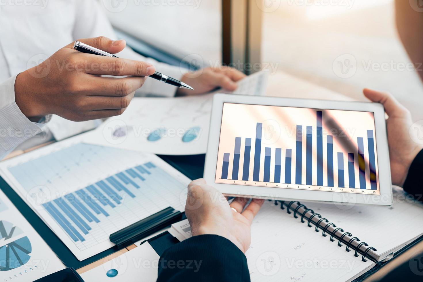 Two business people using digital tablets to analyzing reports of business operating expenses together to summarize note summary information in the office. photo