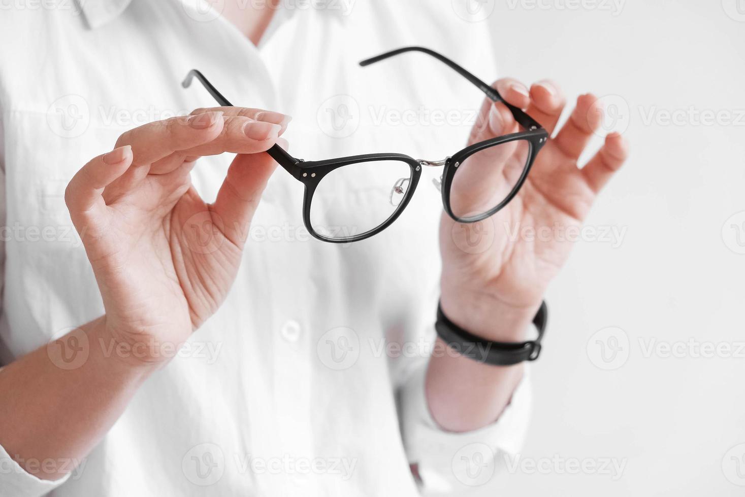 Woman holding optical glasses in a black frame on a white background. Copy, empty space photo