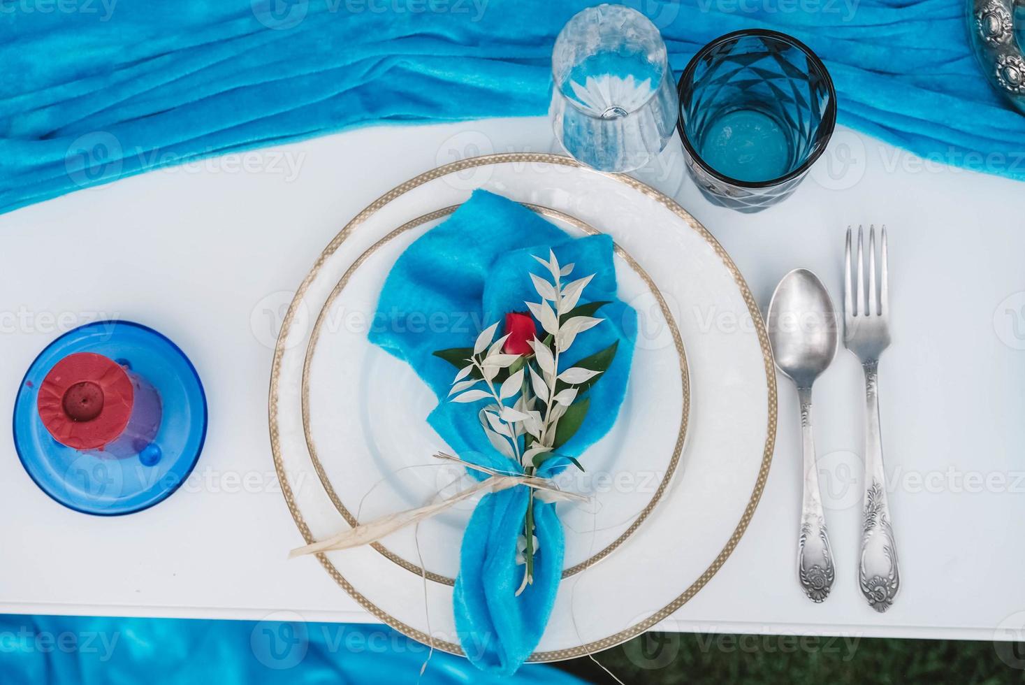 White banquet table covered with blue cloth, served with plates, cutlery, glasses, candles and flower arrangements. Top view. Copy, empty space for text photo