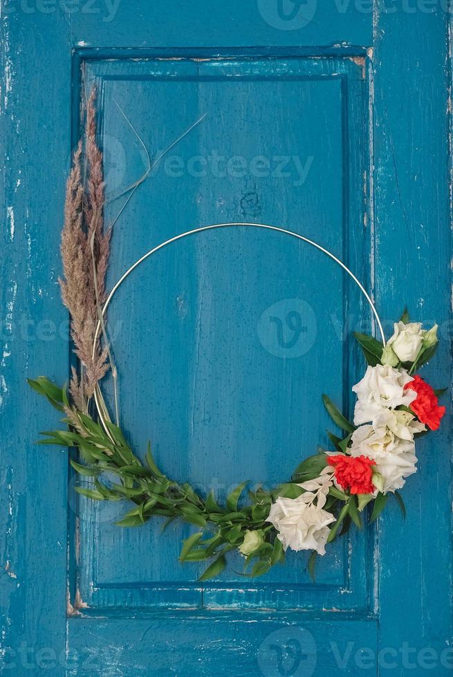 Decorated wreath of flowers, leaves and dry grass on a wooden blue door background. Copy, empty space for text photo