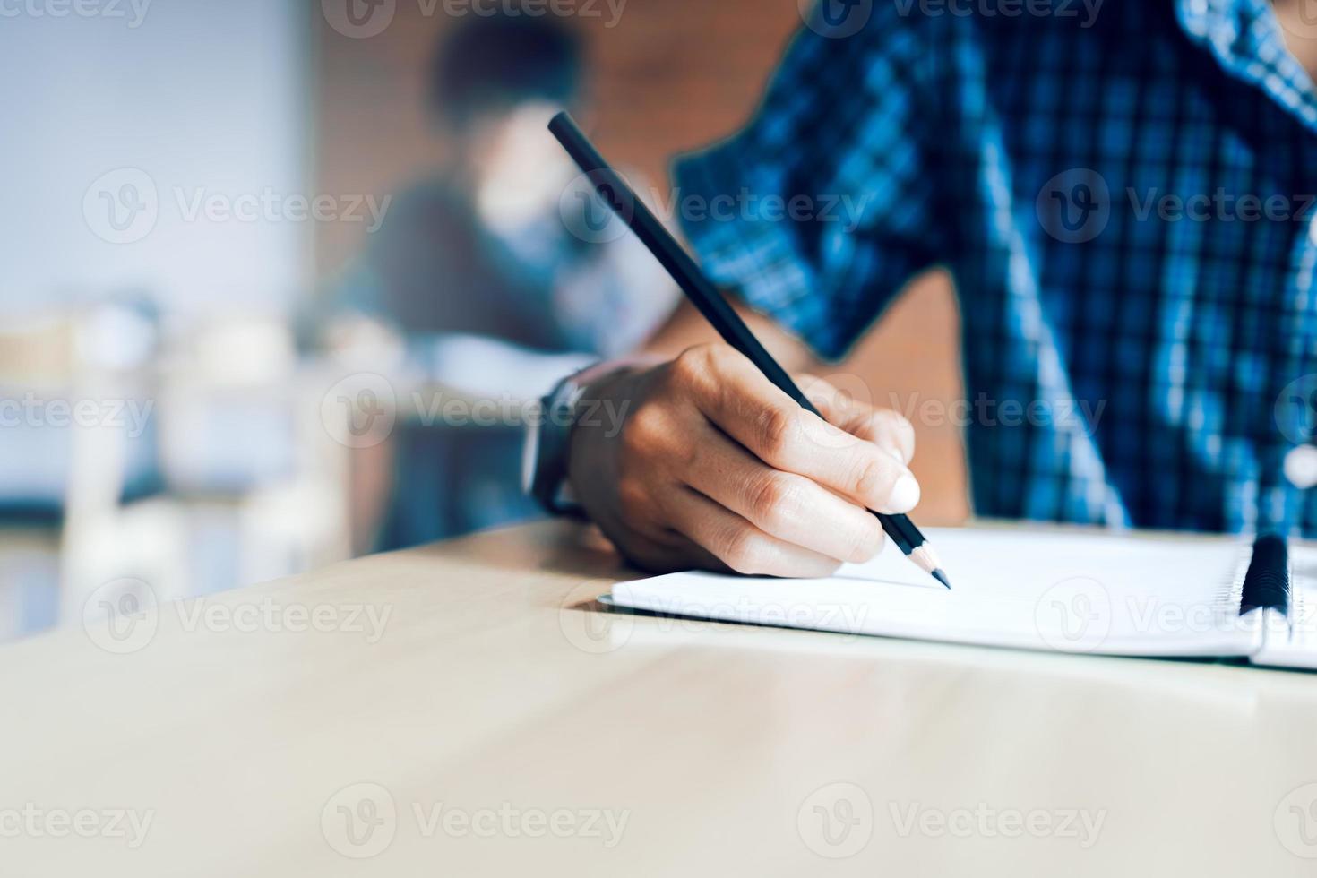 primer plano de la mano de un estudiante adolescente escribiendo en un examen en papel con un lápiz en el aula. foto