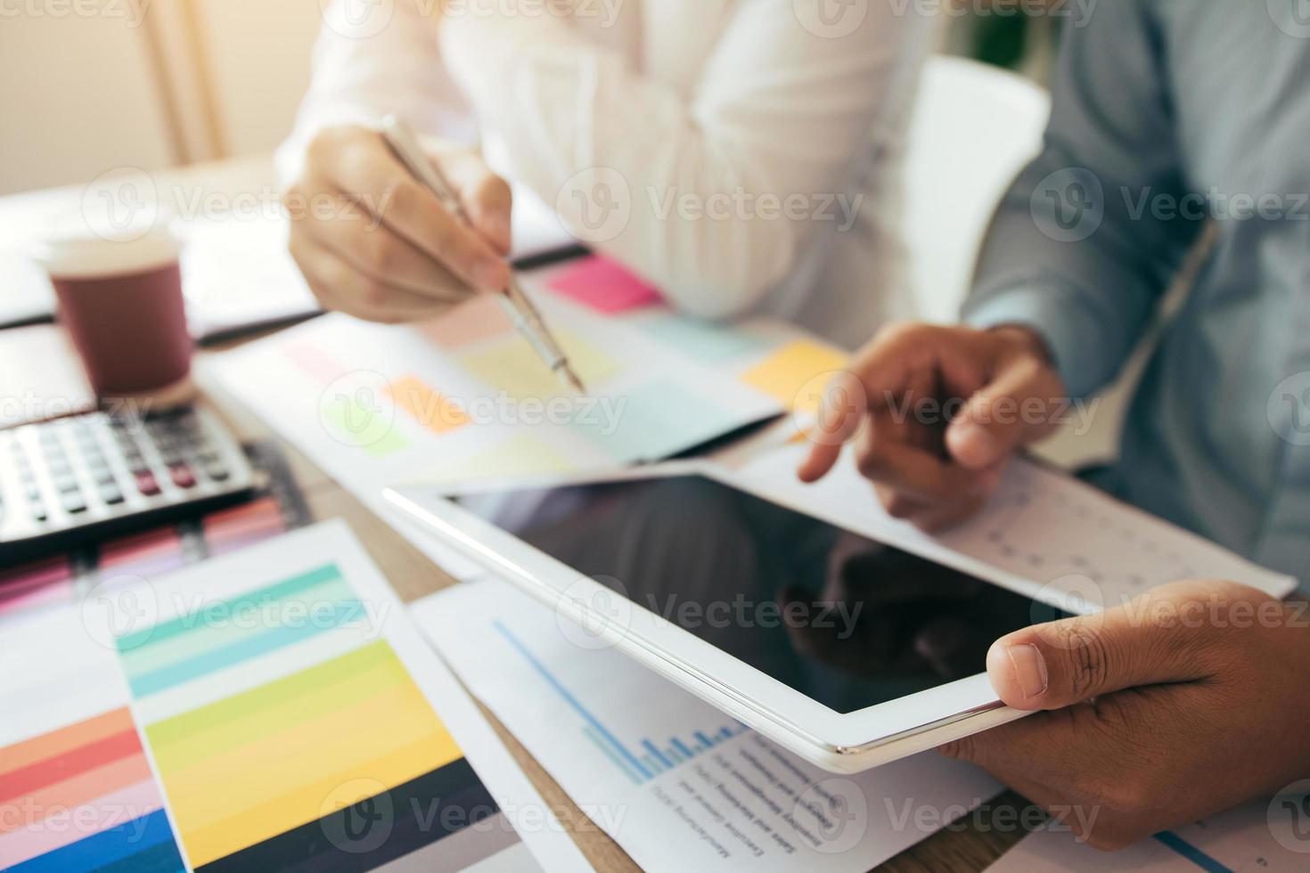 Two business partnership coworkers working on digital tablet discussing a financial planning graph and company during a budget meeting in office room. photo