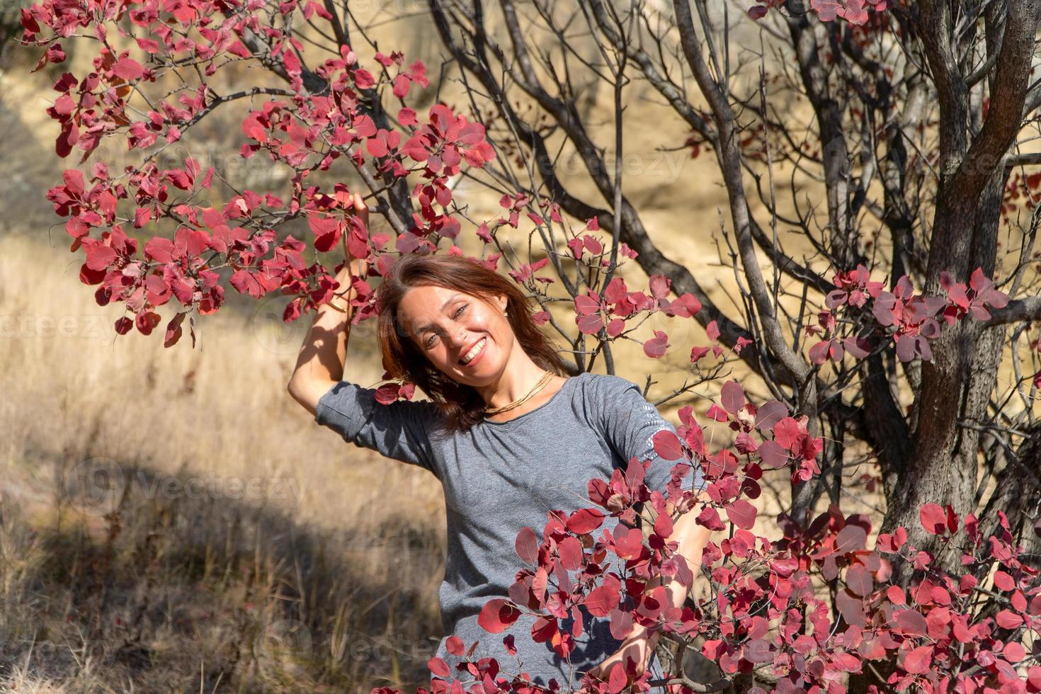 mujer sonriente cerca de un árbol con hojas rojas, retrato de otoño foto