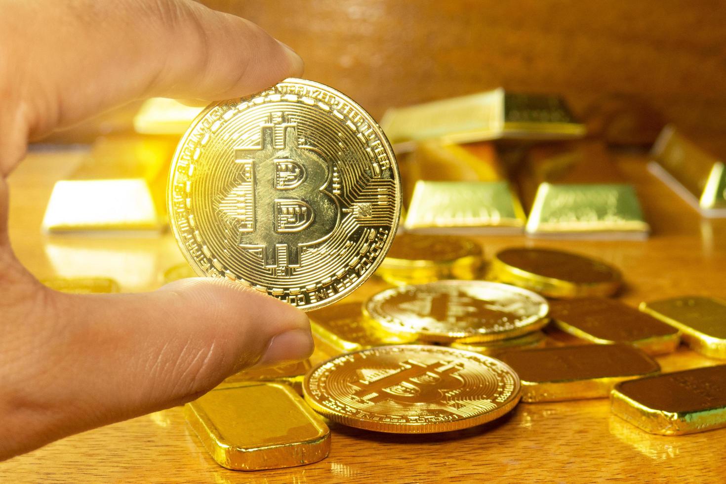 man's hand is picking up bitcoin golden money were laid on the wooden floor. decorate scene with gold bar. They are used for exchange or trading and are a valuable treasure in the investment business. photo