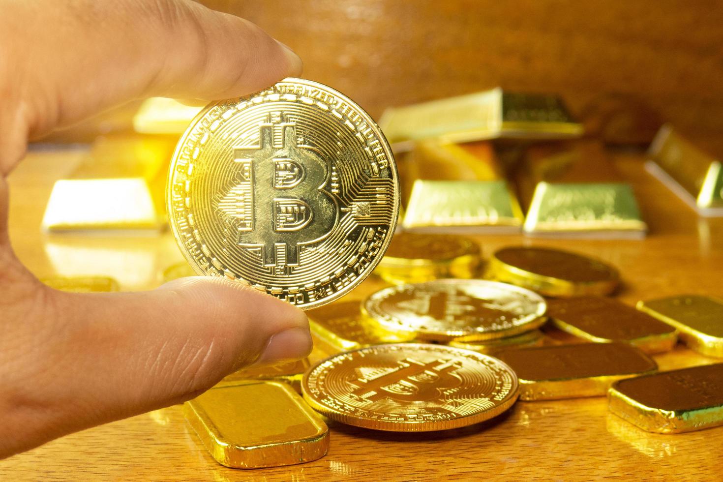 la mano del hombre está recogiendo el dinero dorado de bitcoin que se colocó en el suelo de madera. decorar escena con barra de oro. se utilizan para el intercambio o el comercio y son un tesoro valioso en el negocio de las inversiones. foto