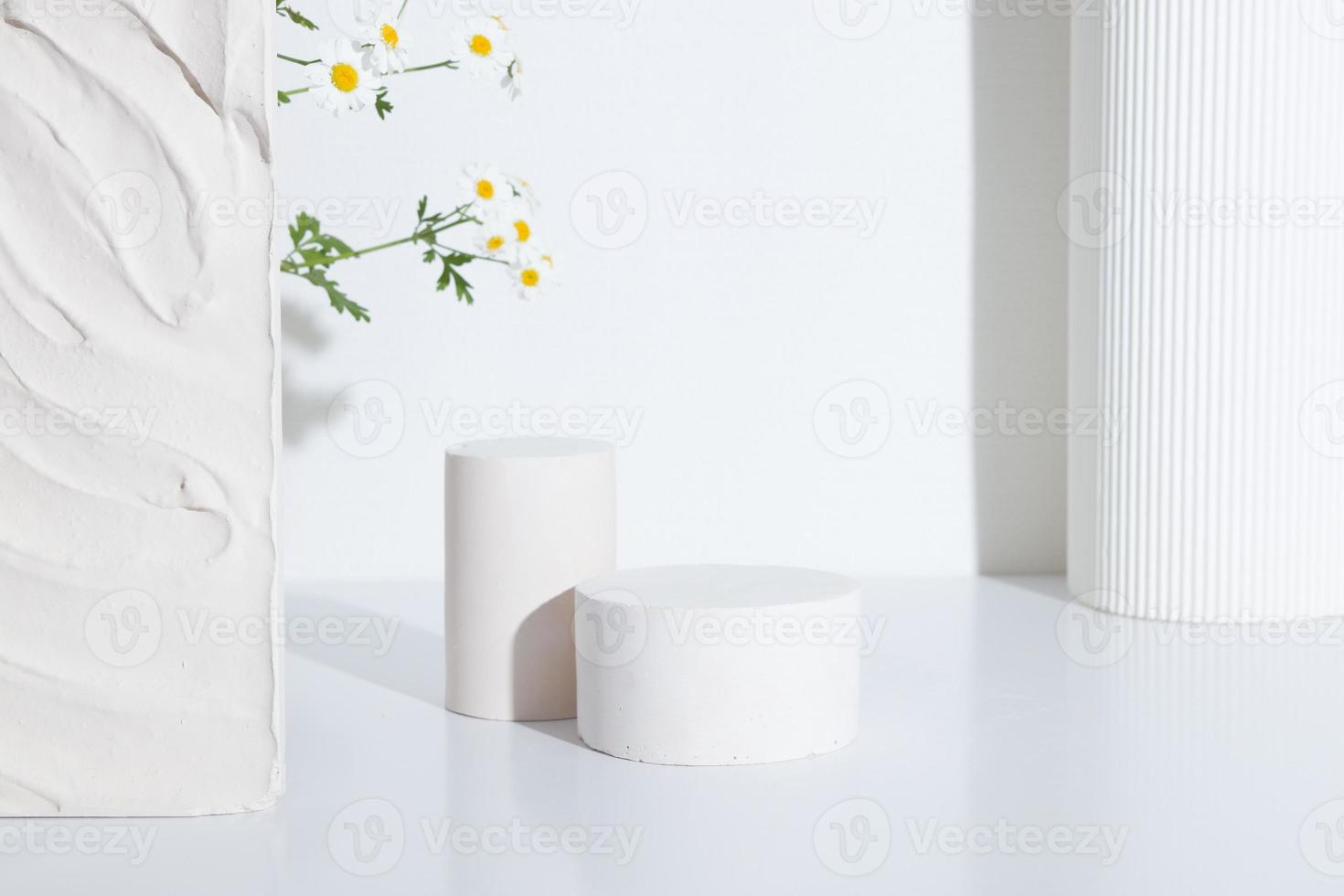 Empty cylindrical podium or pedestal with chamomile flowers on a white background. Blank shelf product standing background photo