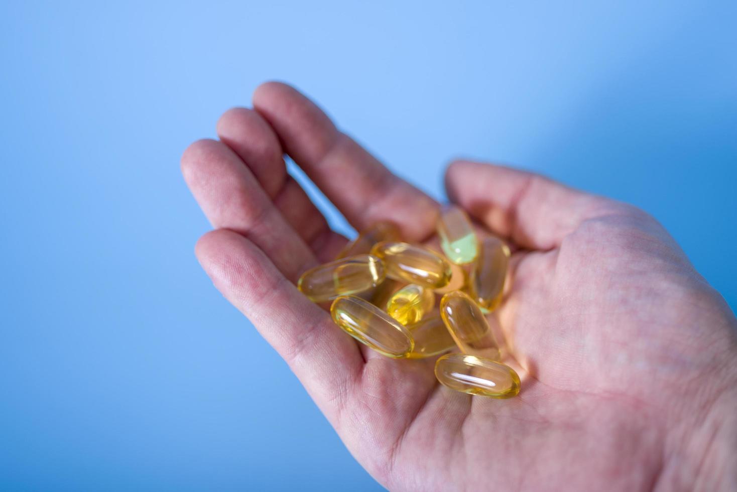 Hand holding omega-3 capsules on a blue background. Palm up, close-up. A high-resolution product. photo