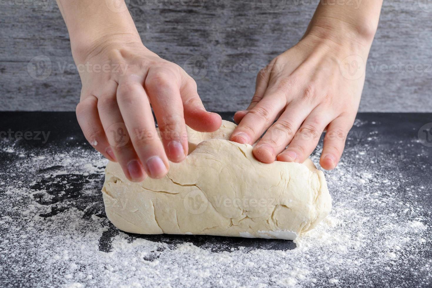 women's hands knead the dough on a wooden table. photo