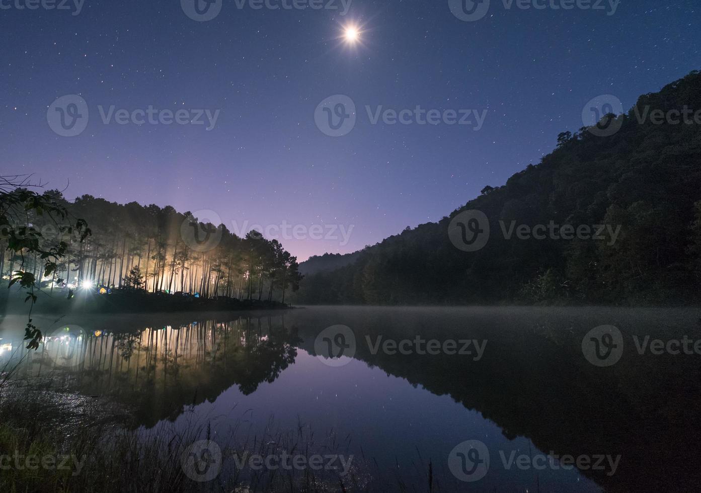 Pine forest light shine with the moon on reservoir at dawn photo