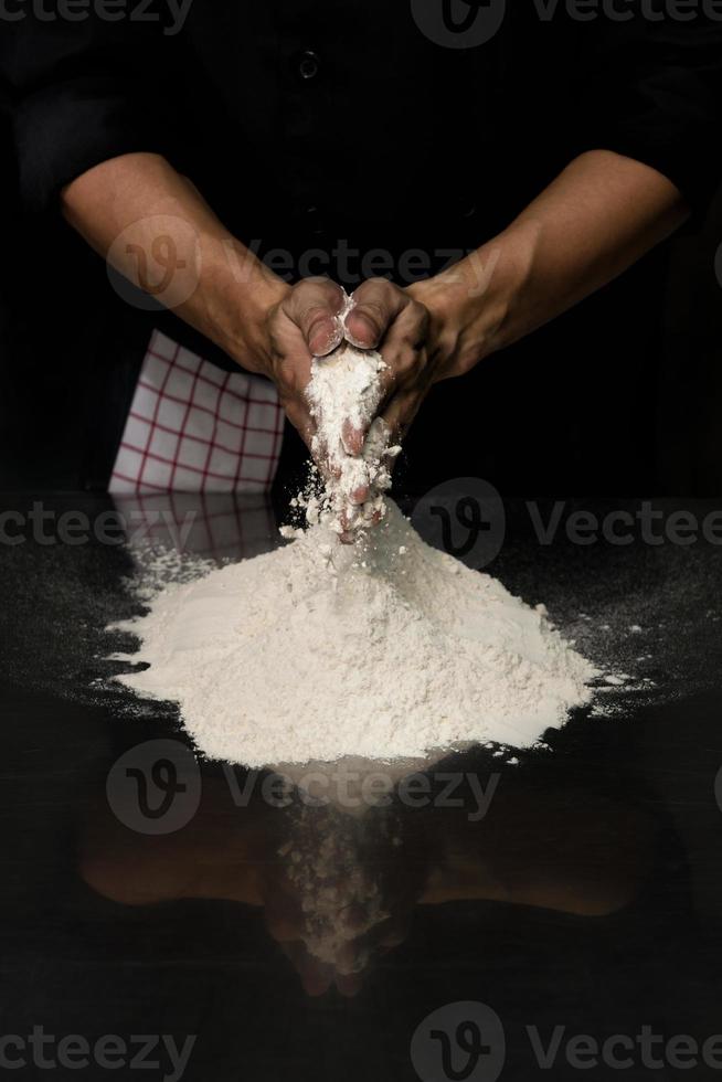 hands chef black cloth knead white flour dough on a table photo