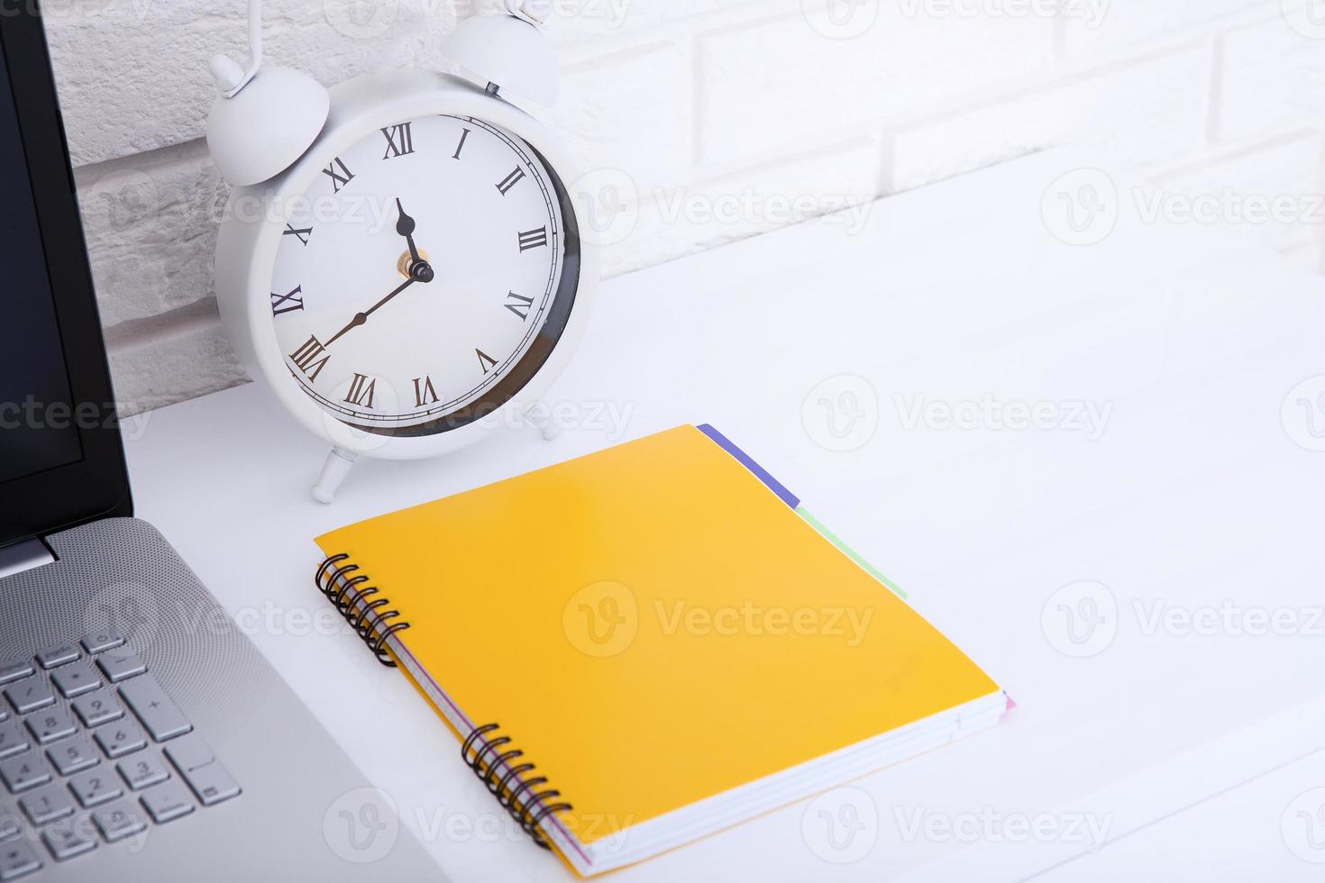 Retro alarm clock with notebook near brick wall on white workplace. Selective focus. Business concept. Copy space photo