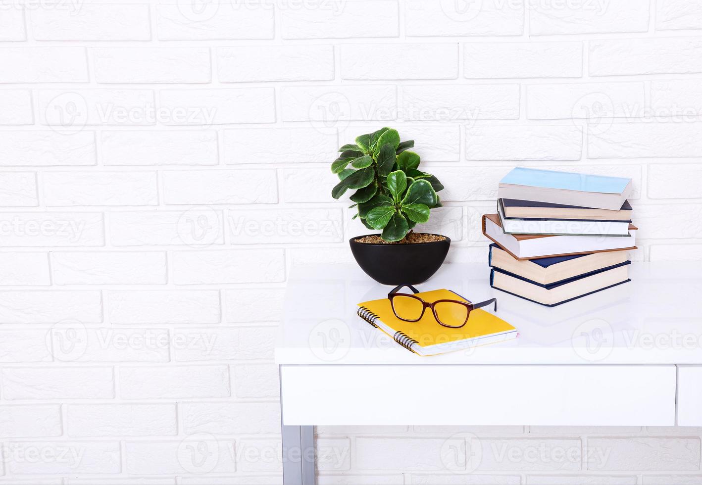 White table near brick wall. Books, notebook and glasses on the workplace. Top view and copy space. Selective focus photo