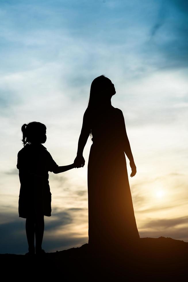 silueta de madre con su hija de pie y puesta de sol foto