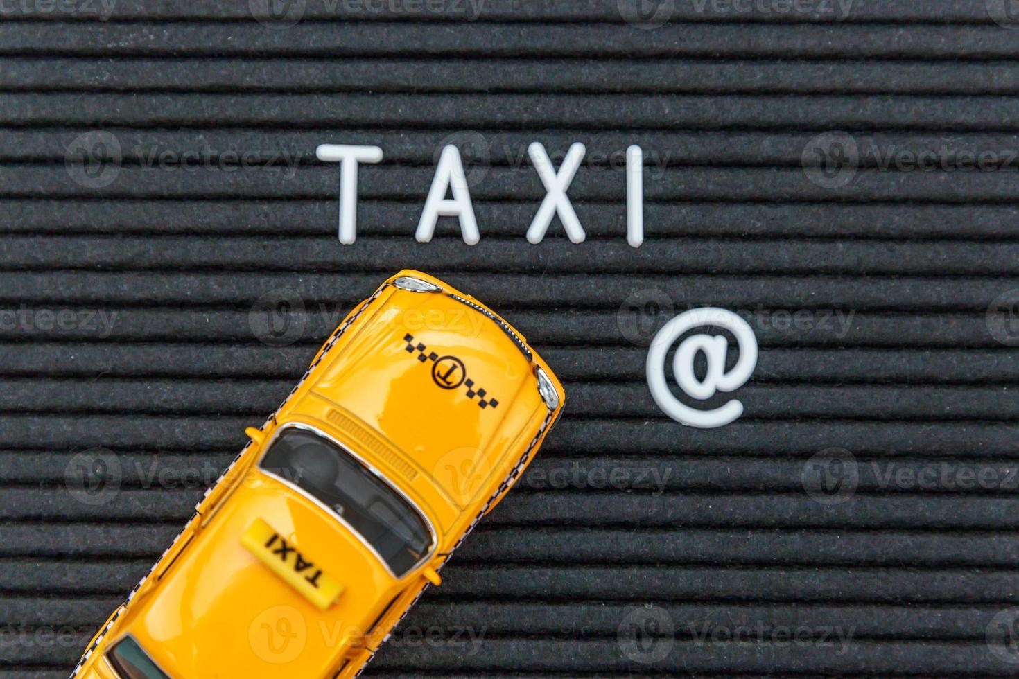 Simply design yellow toy car Taxi Cab model with inscription TAXI letters word on black background. Automobile and transportation symbol. City traffic delivery urban service idea concept. Copy space. photo