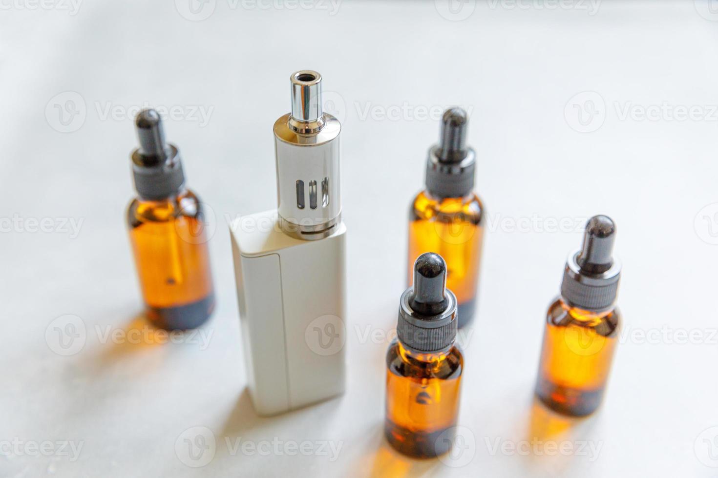 Vaping device e-cigarette electronic cigarette and liquid bottles on concrete stone grey background. Vape device for alternative smoking. Vaping shop concept. Gadget for vaper. Vaping accessories. photo