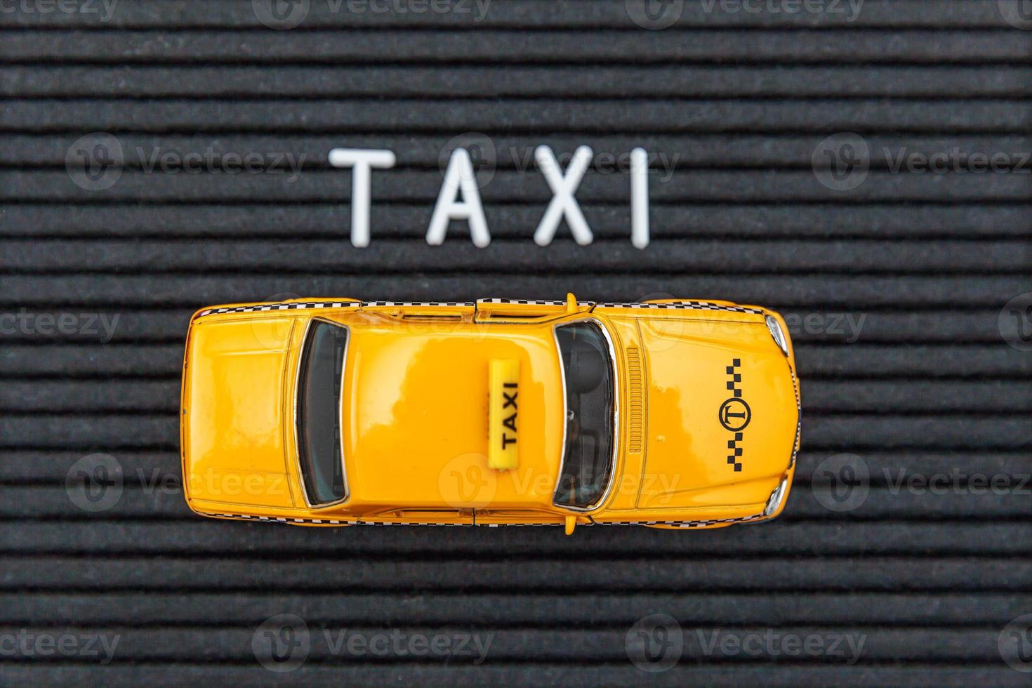 Simply design yellow toy car Taxi Cab model with inscription TAXI letters word on black background. Automobile and transportation symbol. City traffic delivery urban service idea concept. Copy space. photo
