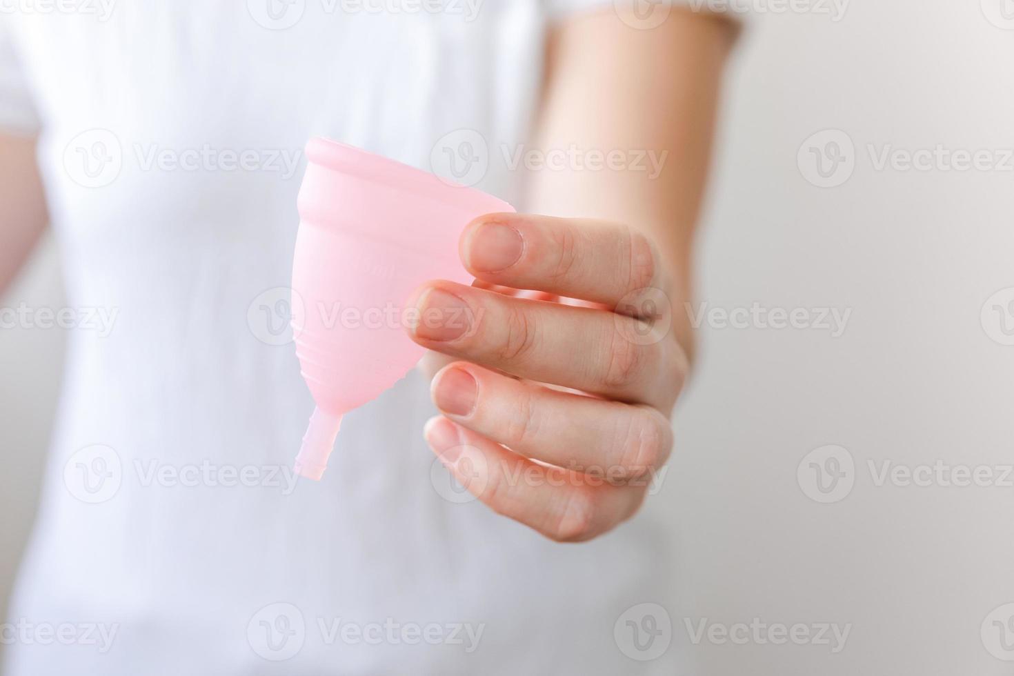 mano de mujer sosteniendo copa menstrual rosa aislada sobre fondo blanco. mujer alternativa moderna eco higiene ginecológica en el período de la menstruación. recipiente para sangre en la mano de una chica. foto