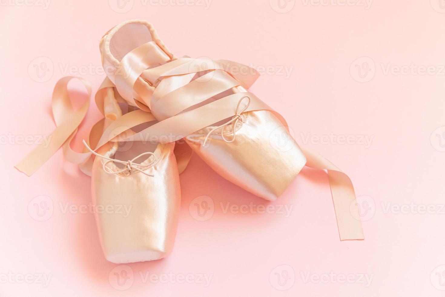 New pastel beige ballet shoes with satin ribbon isolated on pink background. Ballerina classical pointe shoes for dance training. Ballet school concept. Top view flat lay, copy space photo