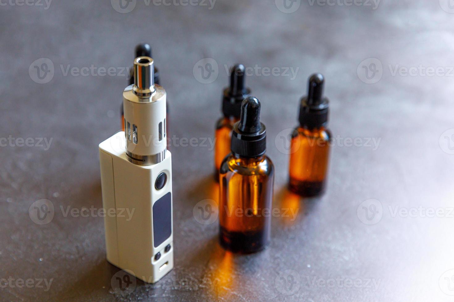 Vaping device e-cigarette electronic cigarette and liquid bottles on dark black stone shale background. Vape device for alternative smoking. Vaping shop concept. Gadget for vaper. Vaping accessories. photo