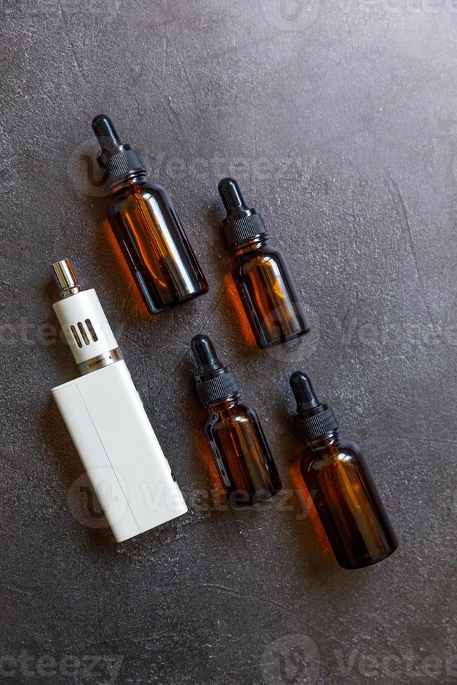 Vaping device e-cigarette electronic cigarette and liquid bottles on dark black stone shale background. Vape device for alternative smoking. Vaping shop concept. Gadget for vaper. Vaping accessories. photo