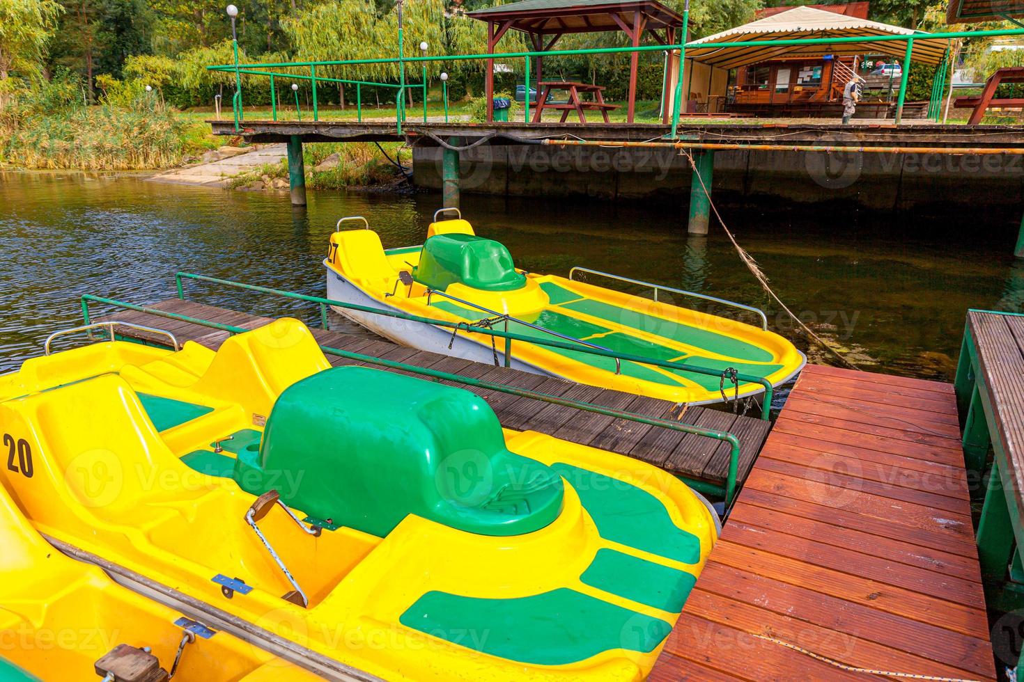 Pedal boats or paddle boats catamarans station. Yellow water bicycles locked at lake marina dock pier on sunny summer day. Summer leisure activity outdoors. photo