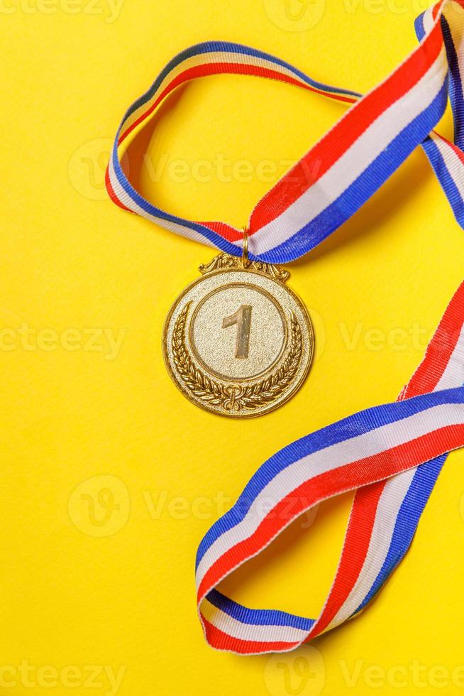 Simply flat lay design winner or champion gold trophy medal isolated on yellow colorful background. Victory first place of competition. Winning or success concept. Top view. photo