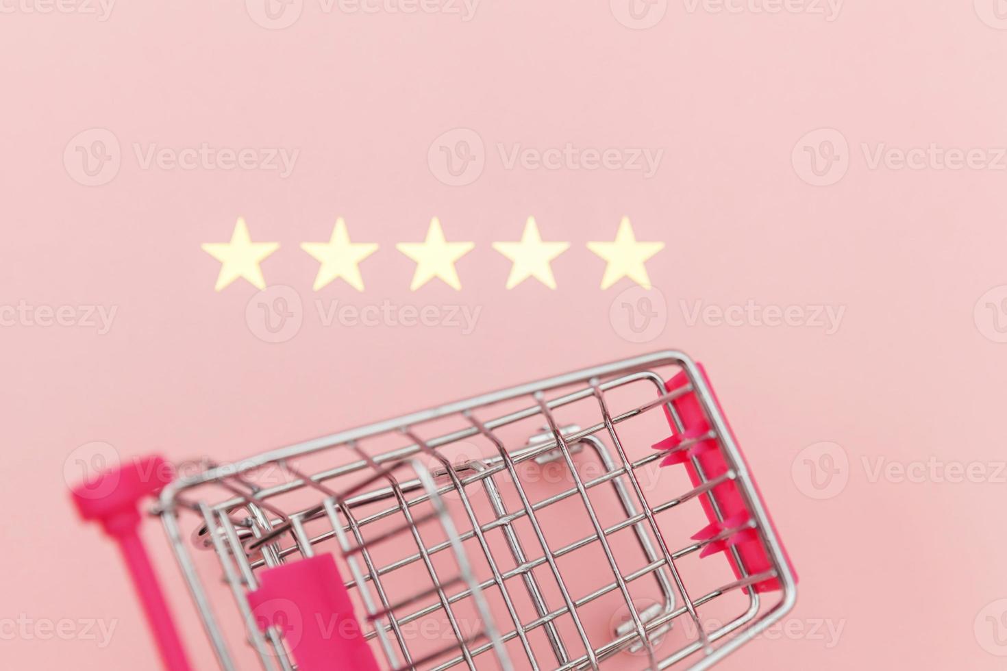 Small supermarket grocery push cart for shopping toy with wheels and 5 stars rating isolated on pastel pink background. Retail consumer buying online assessment and review concept. photo