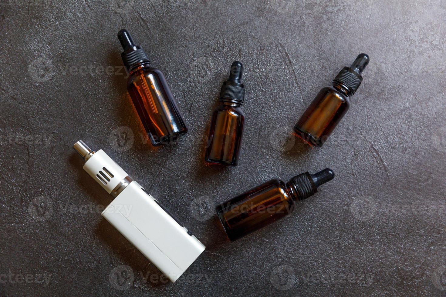 Vaping device e-cigarette electronic cigarette and liquid bottles on dark black stone shale background. Vape device for alternative smoking. Vaping shop concept. Gadget for vaper. Vaping accessories. photo