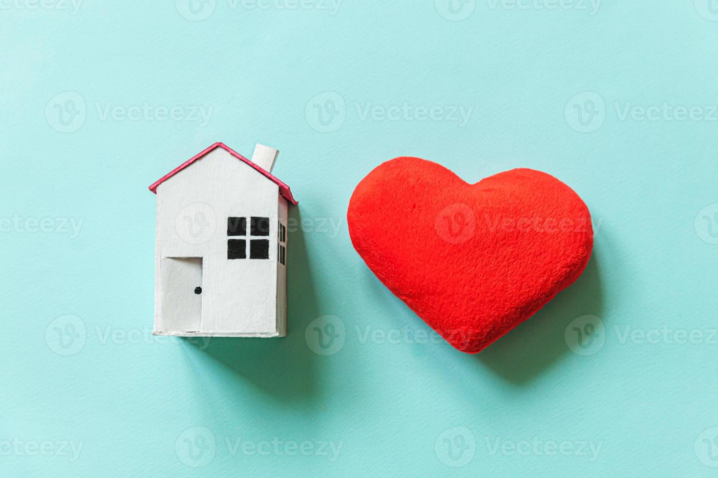 simplemente diseñe con una casa de juguete blanca en miniatura con un corazón rojo aislado en un fondo de moda azul pastel. concepto de casa de ensueño de seguro de propiedad hipotecaria. espacio de copia de vista superior plana. foto