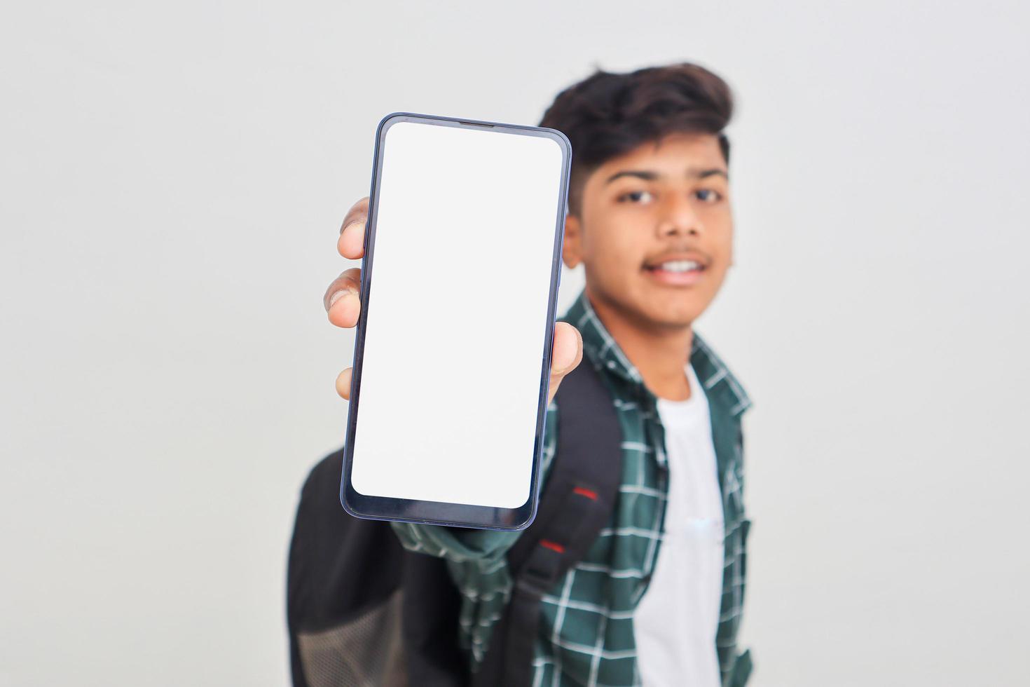 joven estudiante universitario indio que muestra la pantalla del teléfono inteligente con fondo blanco. foto