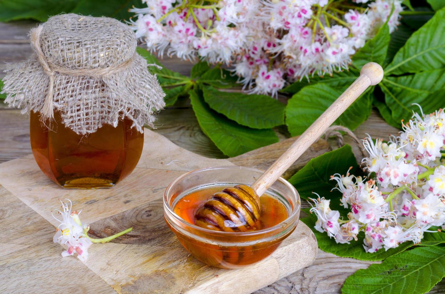 fragante miel de castaño en tarro con flores de flor. foto