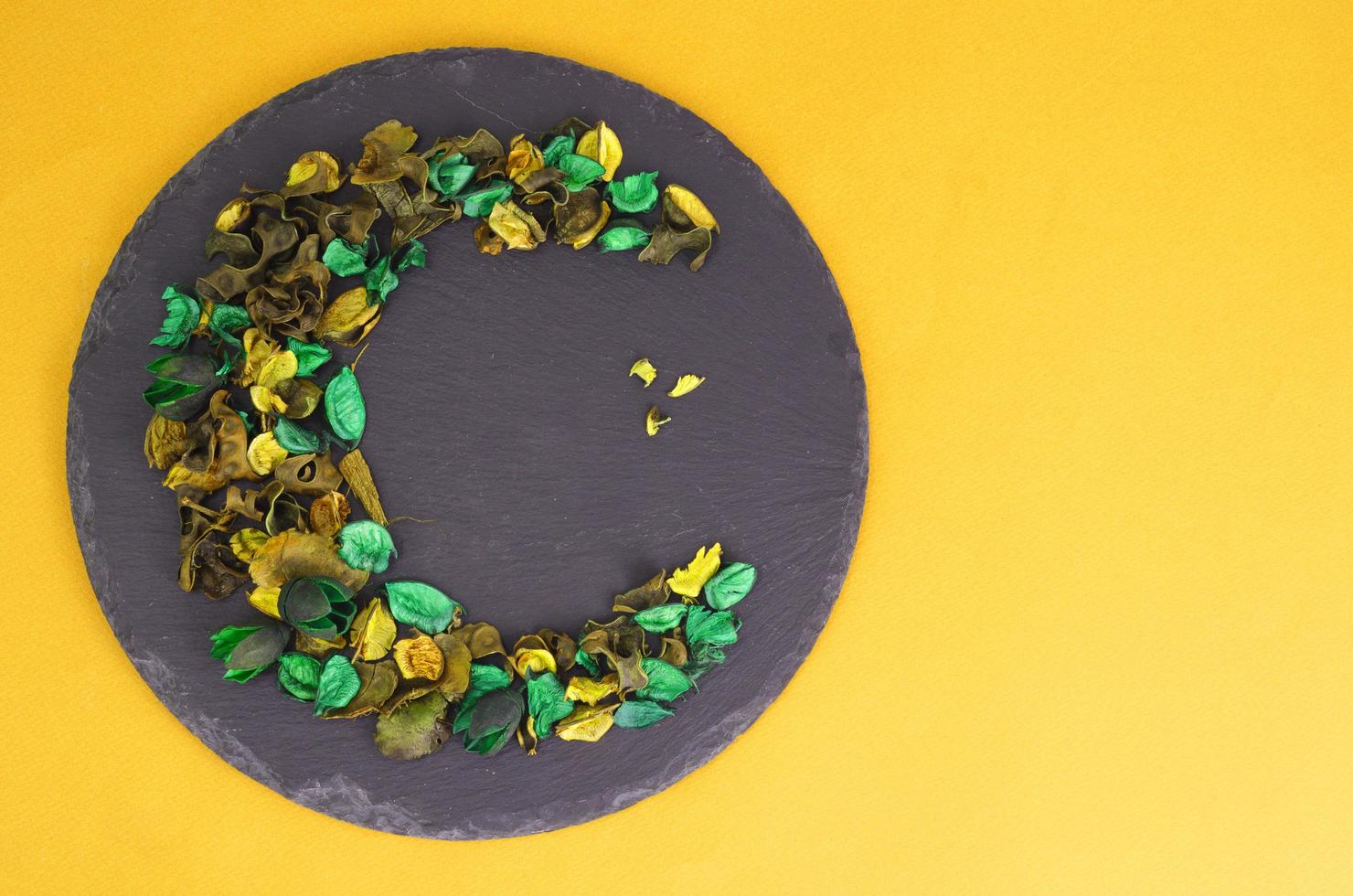 Creative flower composition in form of crescent of dry flowers and petals, green leaves. Top view, flat lay. photo