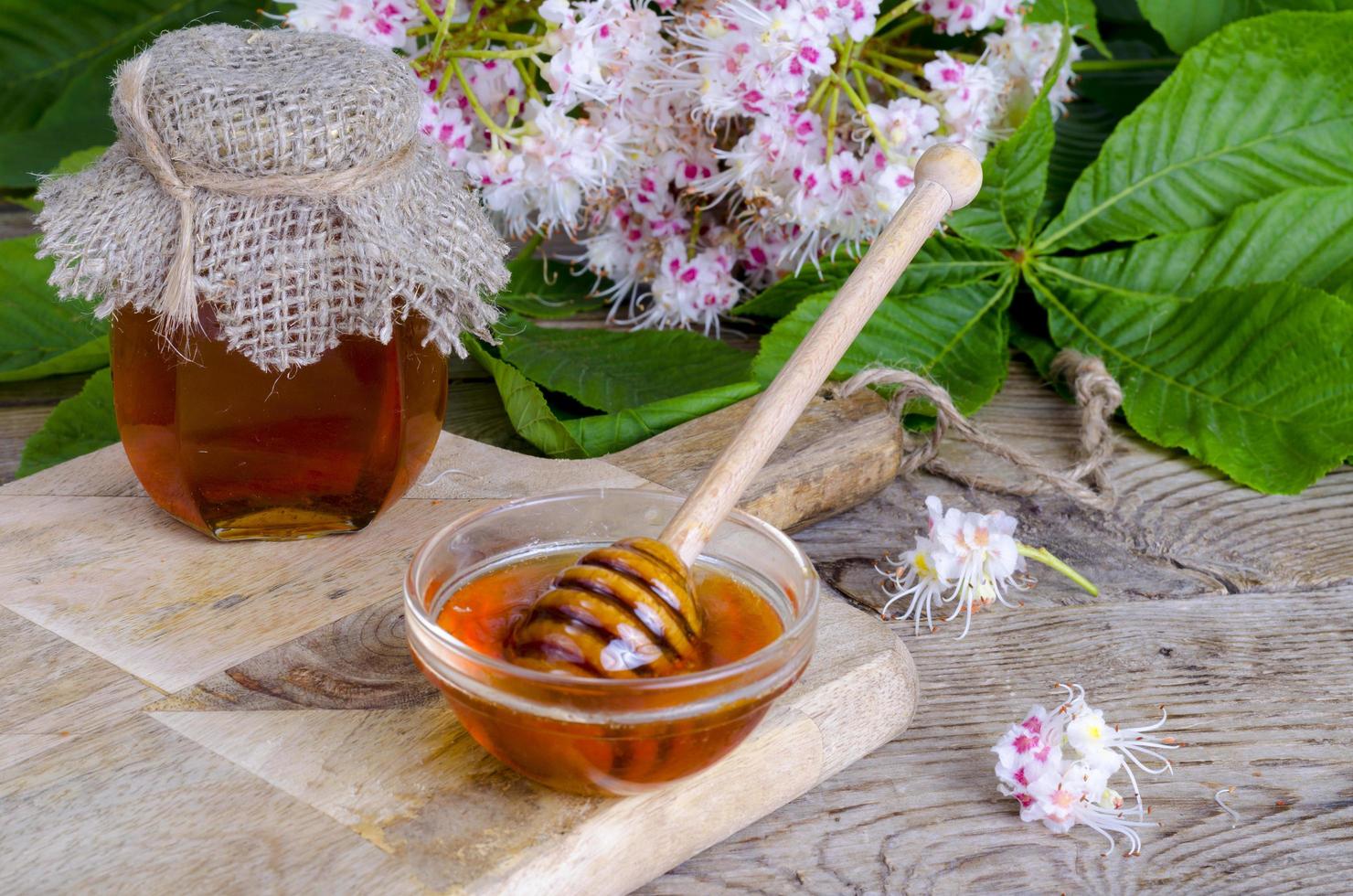 fragante miel de castaño en tarro con flores de flor. foto