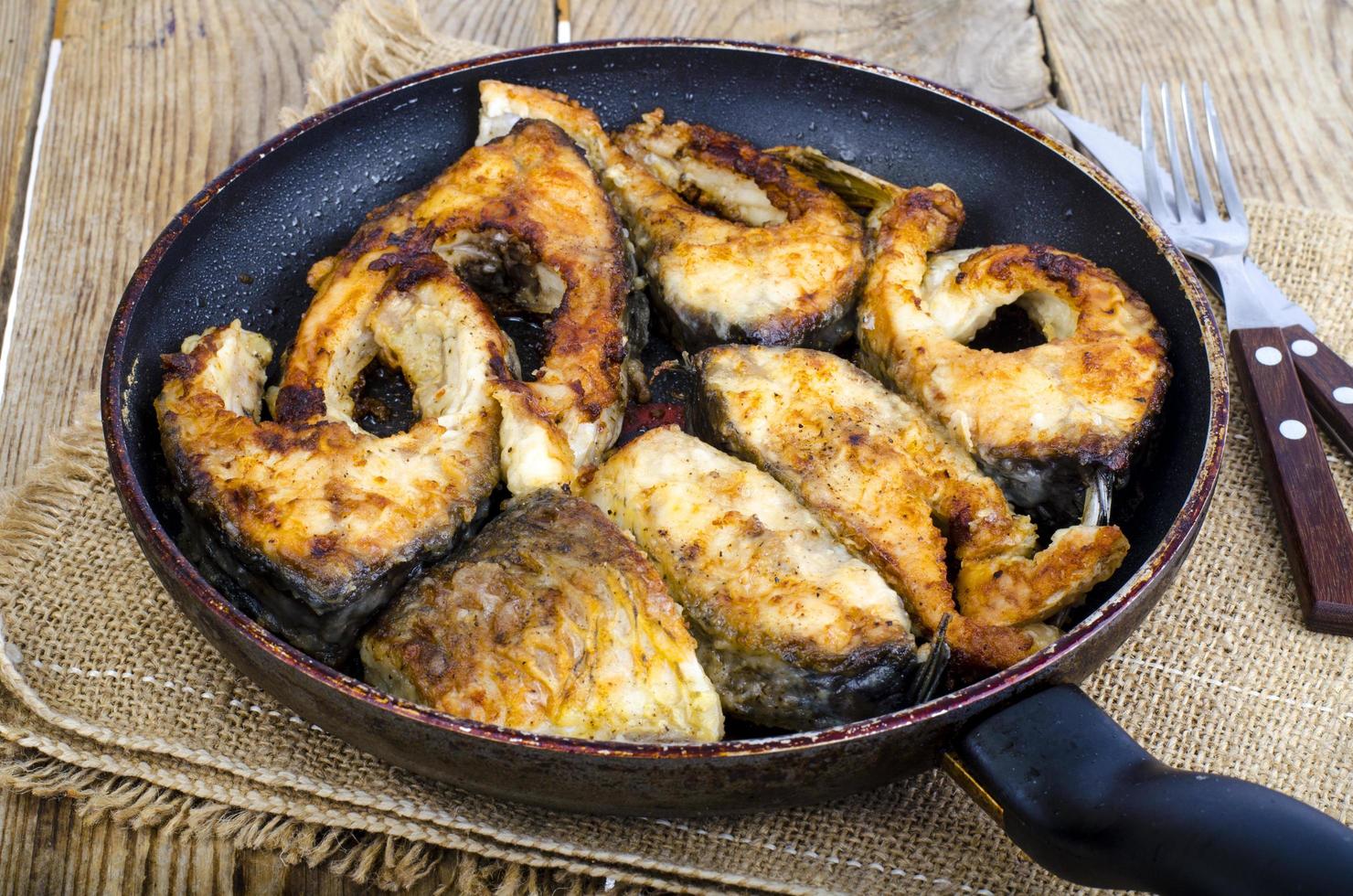 Old frying pan with fried fish on wooden table. photo