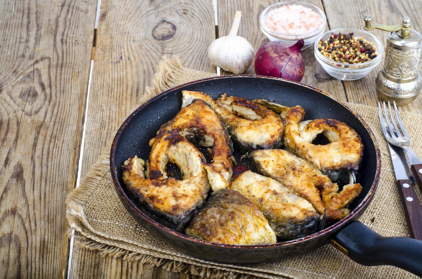 Old frying pan with fried fish on wooden table. photo