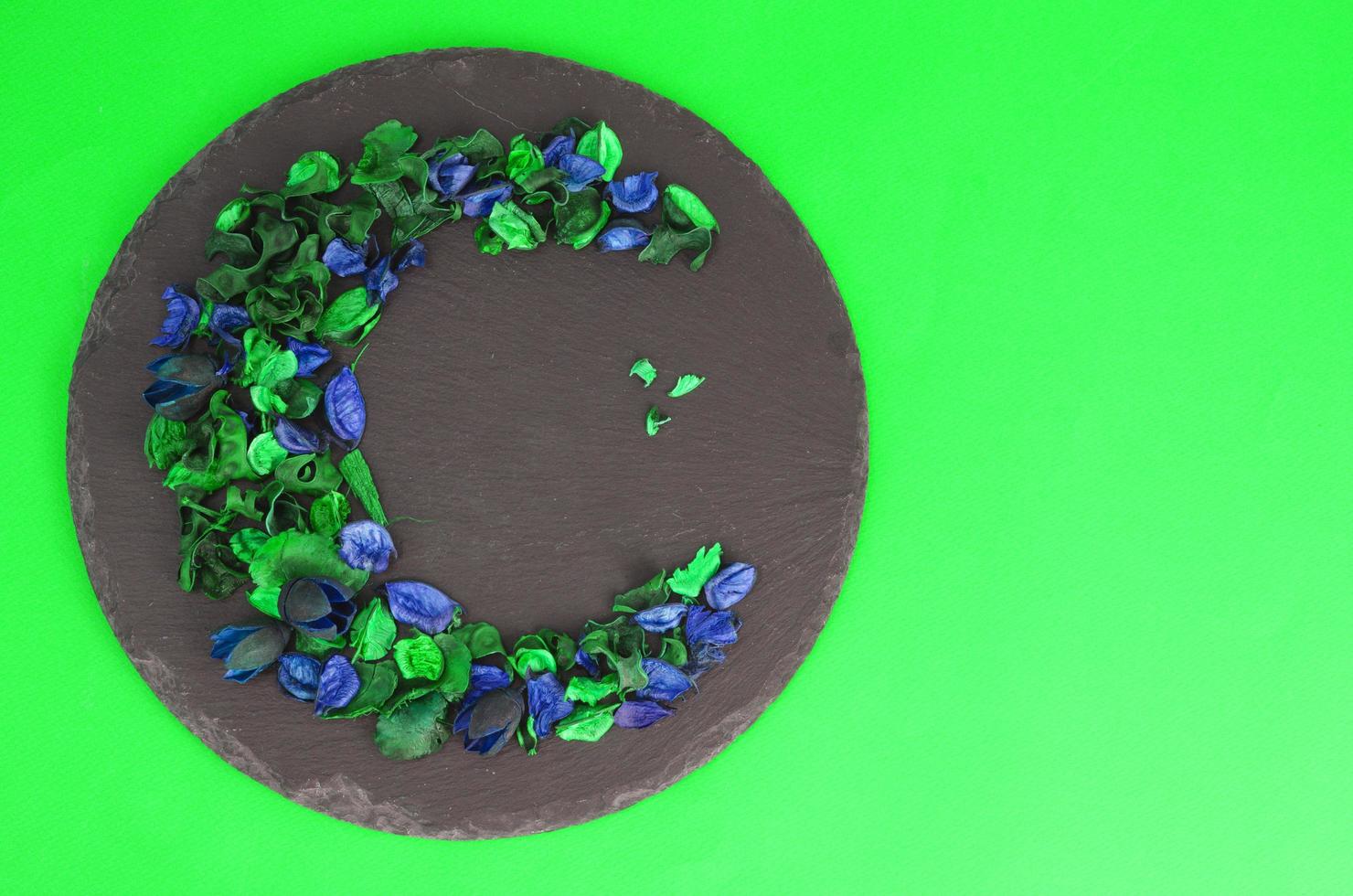 Creative flower composition in form of crescent of dry flowers and petals, green leaves. Top view, flat lay. photo