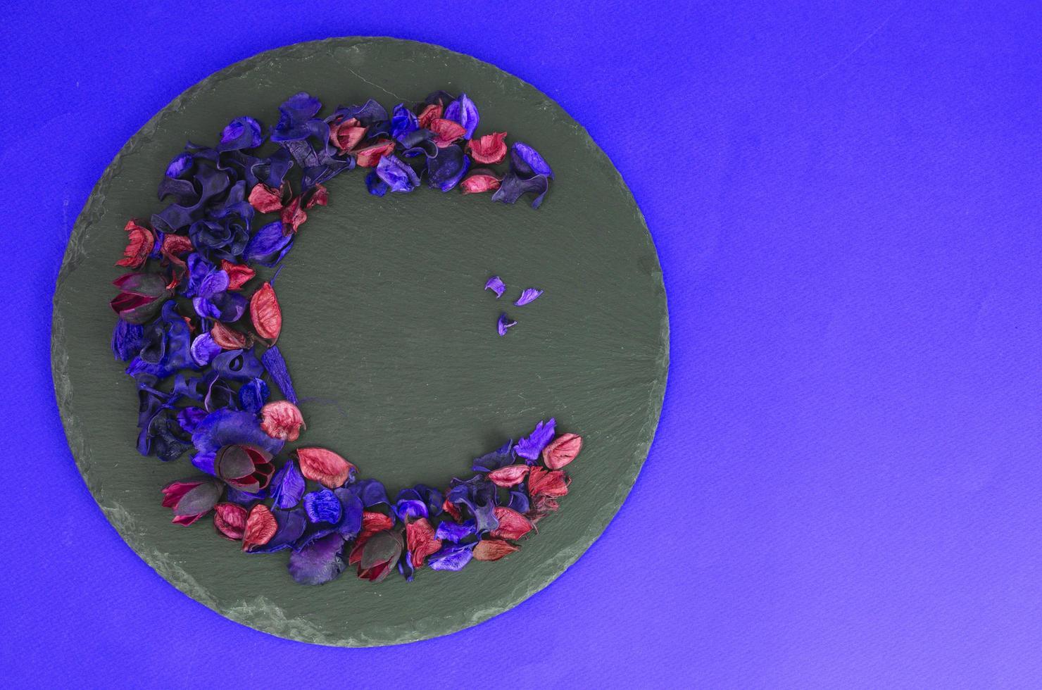 Creative flower composition in form of crescent of dry flowers and petals, green leaves. Top view, flat lay. photo