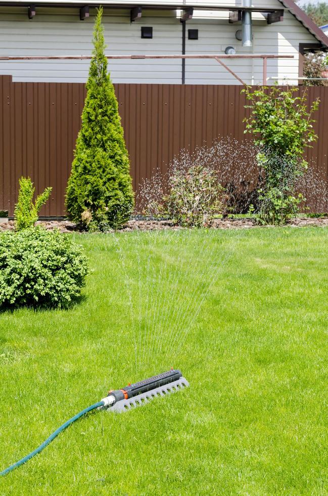 Irrigation system, sprinkler spaying water over green grass lawn photo