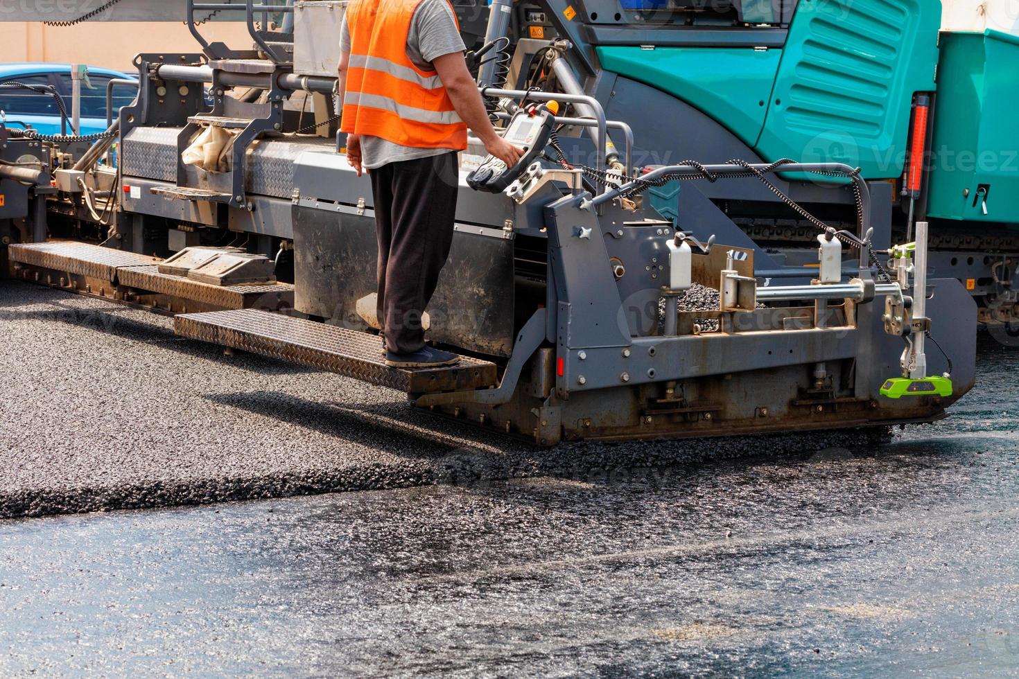 A road worker at the control panel of a tracked paver paver paving fresh asphalt on a fenced road on a summer day. photo