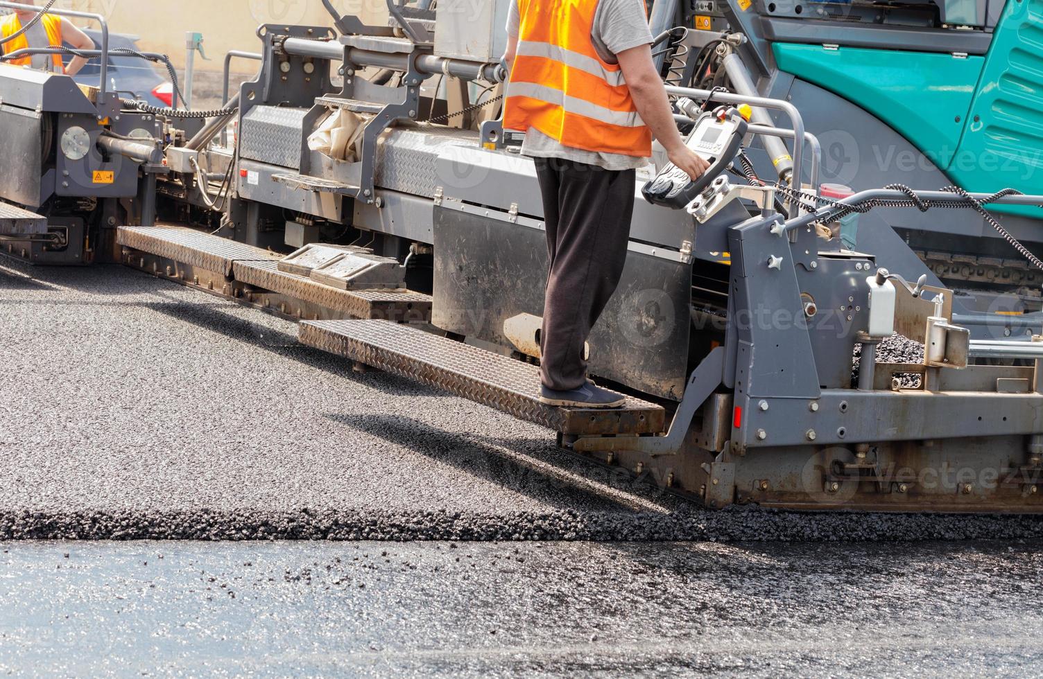 A road worker operates a tracked asphalt paver while paving fresh asphalt on the road on a summer day. photo