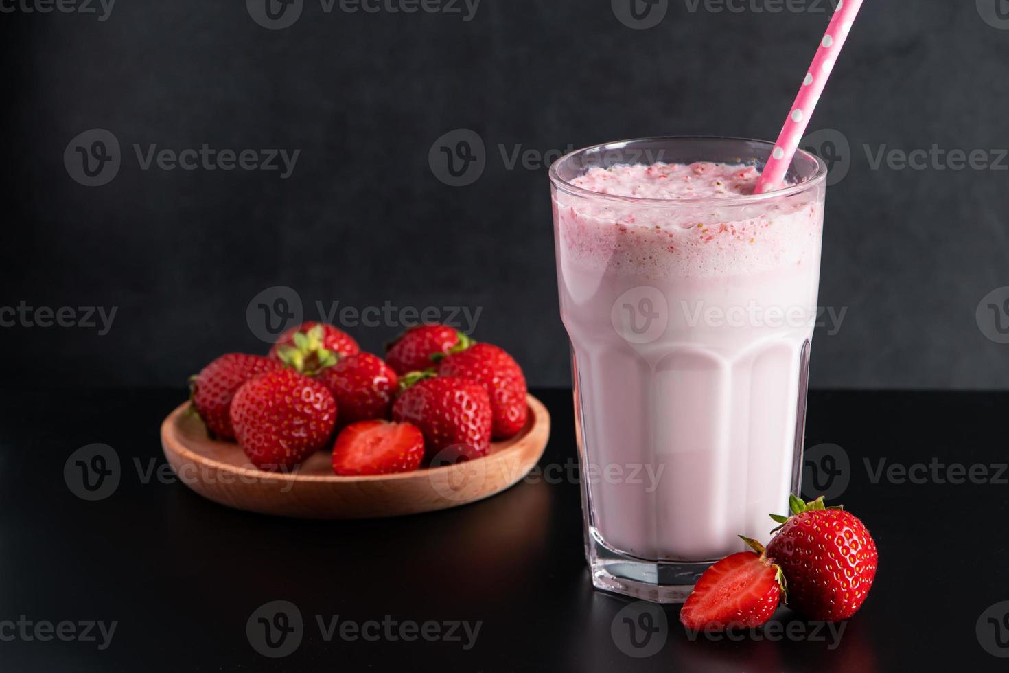 Milkshake with strawberries on black background. Summer drink in a glass with a paper straw. photo
