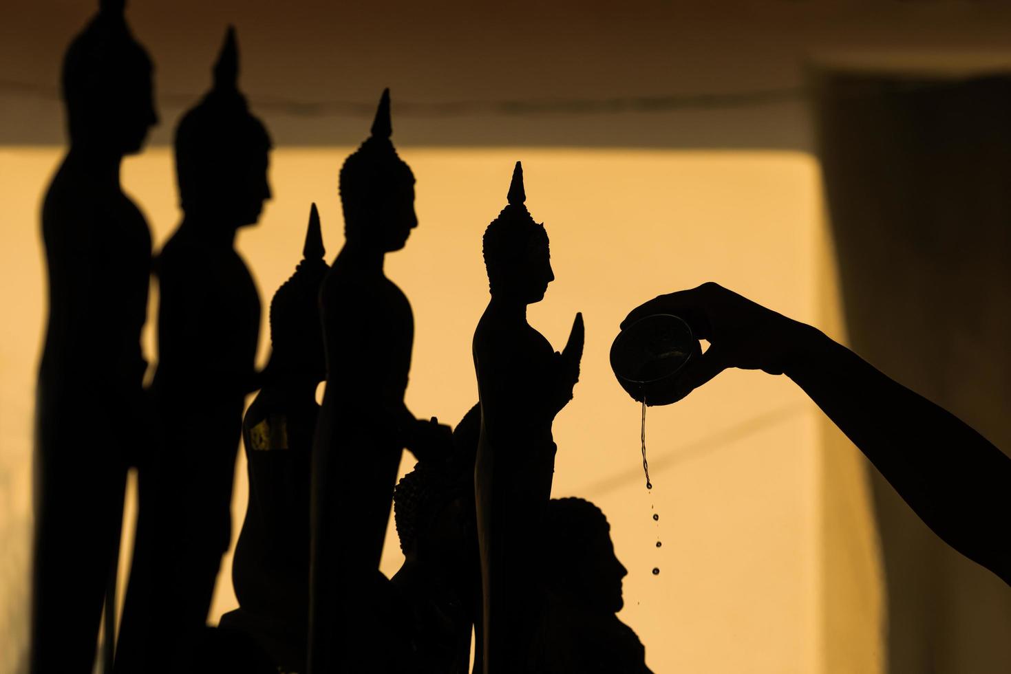silueta de buda vertiendo agua a la estatua de buda en la tradición del festival songkran de tailandia foto
