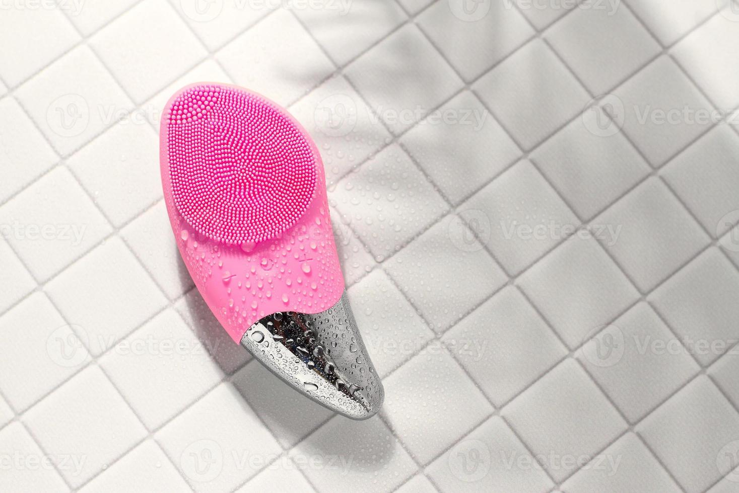 Pink facial sonic brush for massage on white tile with water drops photo