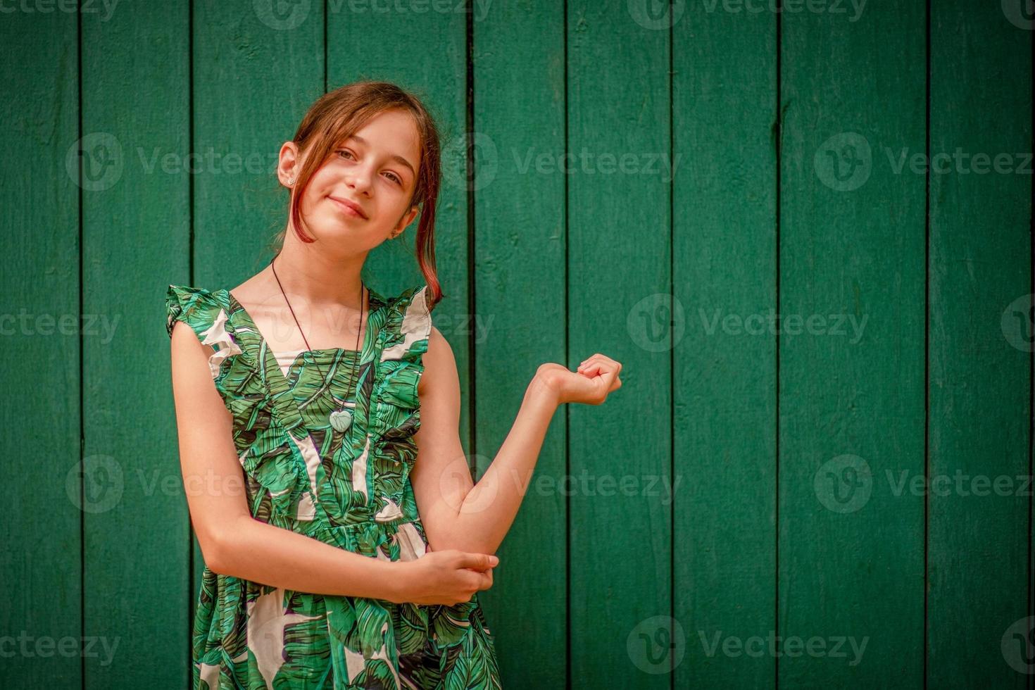 Teen girl portrait in a dress on a green background. Girl 10 or 11 years old on a summer day. photo