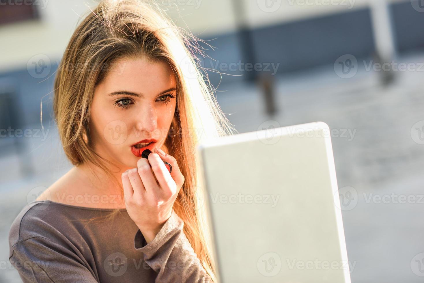 mujer joven aplicando lápiz labial mirando la tableta foto