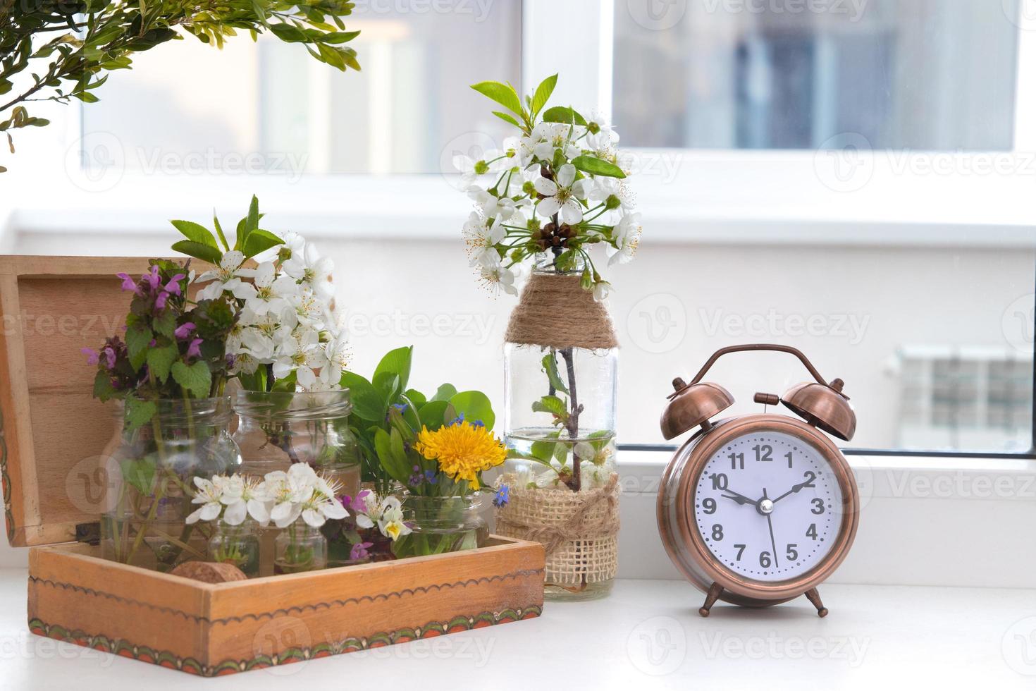 Alarm clock with flowering branches in a wooden box on the windowsill. Spring forward photo